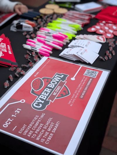A table of swag with a sign to encourage students and employees to play the Cyber Bowl.
